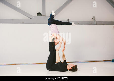 A young Caucasian male and female couple practicing acrobatic yoga in a white gym on mats. They are in the STAR pose. Stock Photo