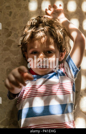 Creative portrait of a child with a pattern of lights and shadows on his face created to pass sunlight through a window. Stock Photo