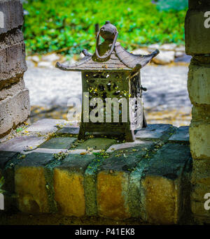 Old Japanese style iron lantern sits on old brick wall in garden area Stock Photo
