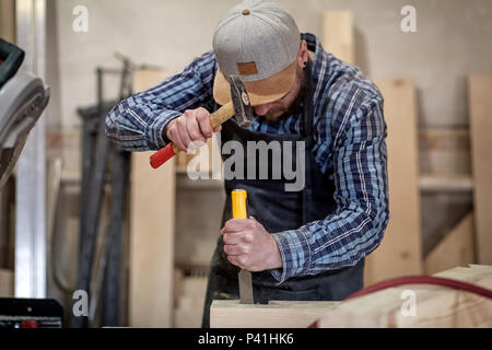 Close up experienced carpenter in work clothes and small buiness owner working in woodwork workshop,  using chisel for cutting out of wood  in worksho Stock Photo