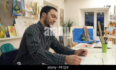 Male art student making a sketch with a pencil sitting at the desk in studio Stock Photo