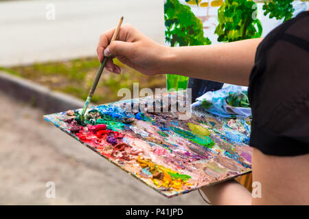 A close-up artist paints on a canvas an urban landscape of a summer embankment with atractions of oil paints Stock Photo