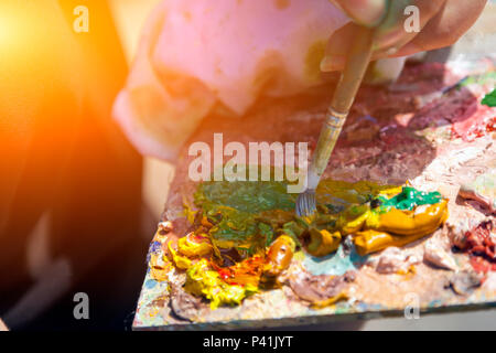 A close-up artist paints on a canvas an urban landscape of a summer embankment with atractions of oil paints Stock Photo