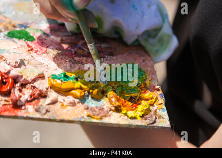 A close-up artist paints on a canvas an urban landscape of a summer embankment with atractions of oil paints Stock Photo