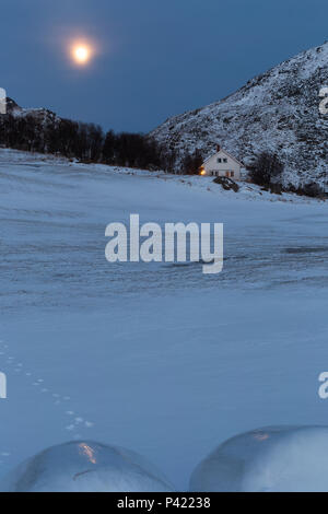 A house on snowy mountain under full moon. Winter evening at Haukland, Lofoten, Nordland, Norway Stock Photo