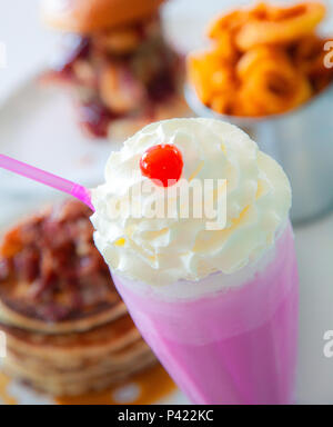 Pink Strawberry Milkshake with burger and fries in the background Stock Photo
