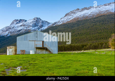 A barn on a grassland near mountains covered in snow, and a flock of sheep grazing nearby. Stock Photo