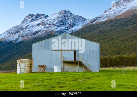 A barn on a grassland near mountains covered in snow, and a flock of sheep grazing nearby. Stock Photo