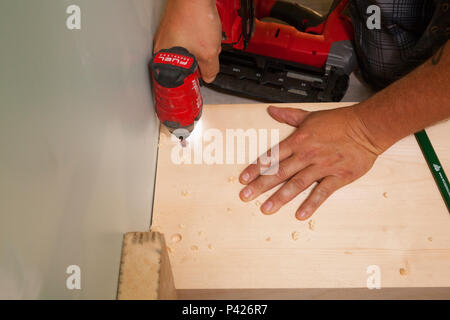 A construction worker using a battery operated drill to install screws into a wooden stairwell in Ontario, Canada. Stock Photo