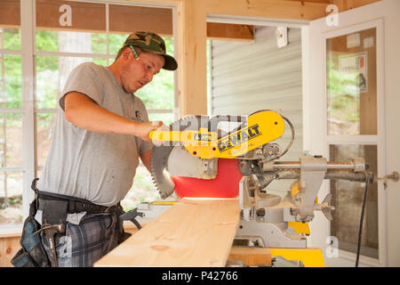 A construction worker using a circular saw to cut a wooden plank in Ontario, Canada. Stock Photo
