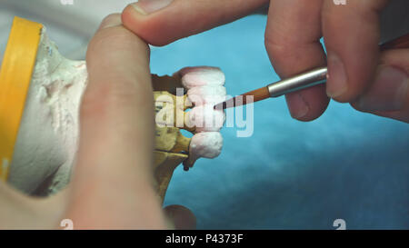 Dental technician applying ceramics glaze to a cast made with CNC dental machine Stock Photo