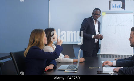 Colleagues asking a question to a businesswoman during a presentation Stock Photo