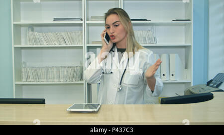 Young stressed woman yelling and gesturing while speaking on telephone at hospital reception Stock Photo