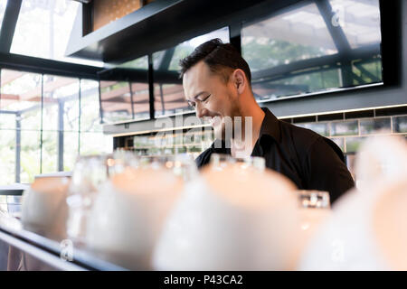 Happy young man working as barista behind the bar counter Stock Photo