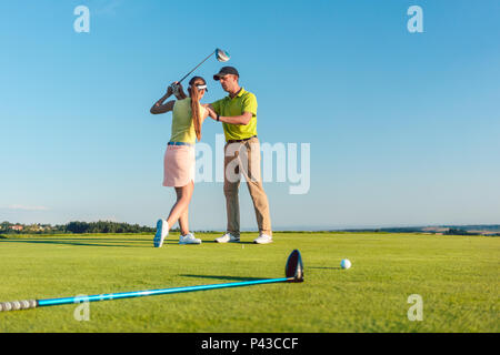 Golf instructor teaching a young woman to swing the driver club  Stock Photo