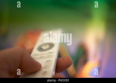 Extreme close up shot of a hand holding a television remote control and pointing it at a television set to change the channel Stock Photo