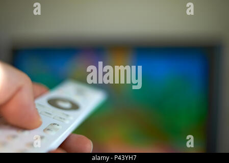 Extreme close up shot of a hand holding a television remote control and pointing it at a television set to change the channel Stock Photo