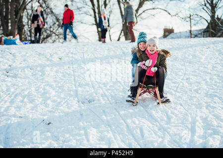 Two girls are sledding down a hill in the neighborhood together in the snow. Stock Photo