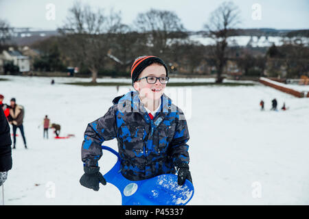 Little boy is walking back up a big hill after sledding down it in the snow. Stock Photo