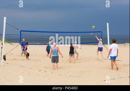 People having fun playing beach volleyball at Sandbanks beach under dark grey stormy skies, Poole, Dorset in May Stock Photo