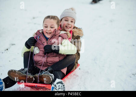 Two little girls are going down a snowy hill together on a sleigh. Stock Photo