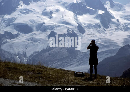 A climber studying a prospective route on a mountain with binoculars, Swiss Alps Stock Photo