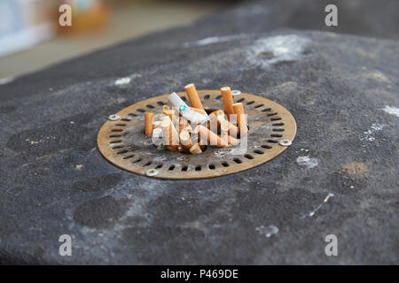 A number of used cigarettes pushed into a metal ashtray built into a waste bin with the butts showing Stock Photo