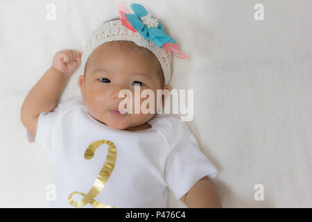 Close - Up Two month old new born asian cute baby rests happily on white bed background. Stock Photo