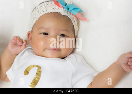 Close - Up Two month old new born asian cute baby rests happily on white bed background. Stock Photo