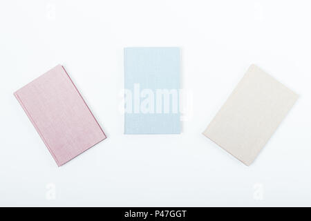 Minimal flat lay composition of three books: pink, blue and beige on a white background. Notebooks with blank covers, top view. Stock Photo