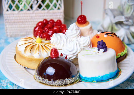 A variety of cakes on a white plate stand on a decorated table. Stock Photo