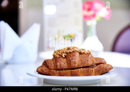 Croissant with a filling on a white plate on a table with flowers in the sunlight. Stock Photo