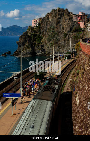 Overhead view of train arriving in Manarola station with waiting tourists and cliffside homes Stock Photo