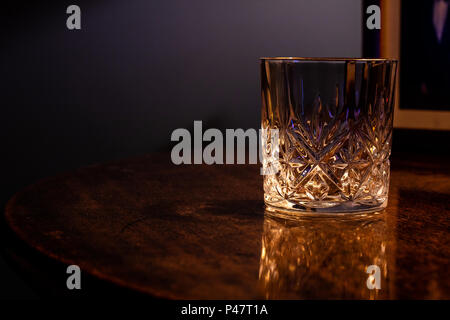 An empty crystal glass resting on on a table with a dark wood grain Stock Photo