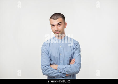 Portrait of happy fashionable handsome man in blue shirt crossing hands and look at camera. He is confident. Eyebrow moving up Stock Photo