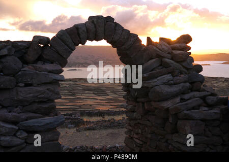 The sun begins to set on a beautiful stone archway on Taquile Island in Lake Titicaca Peru Stock Photo