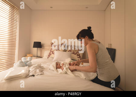 Smiling young mother changing baby diaper on bed in bedroom Stock Photo