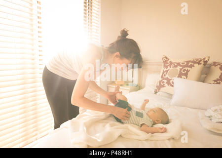 Cute little baby getting dressed by her mother on bed in the bedroom Stock Photo