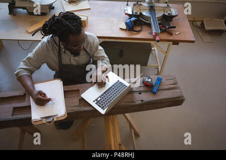 High angle view of carpenter writing in clipboard while using laptop Stock Photo