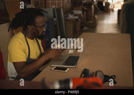Carpenter eating sandwich while working on laptop Stock Photo