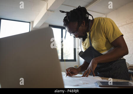 Carpenter writing in paper while using laptop at table Stock Photo
