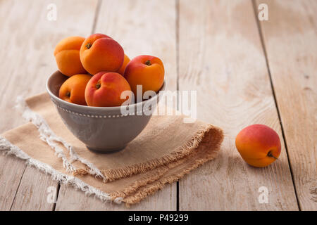Pretty bowl of apricots on rustic backdrop with extra fruit in background Stock Photo