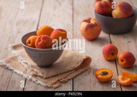 Pretty bowl of apricots on rustic backdrop with extra fruit in background Stock Photo
