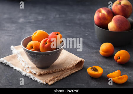 Pretty bowl of apricots on rustic backdrop with extra fruit in background Stock Photo