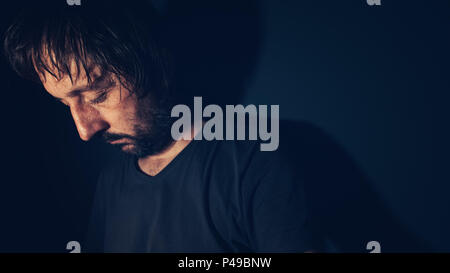 Mental health and depression concept, sad depressed man sulking in dark interior Stock Photo