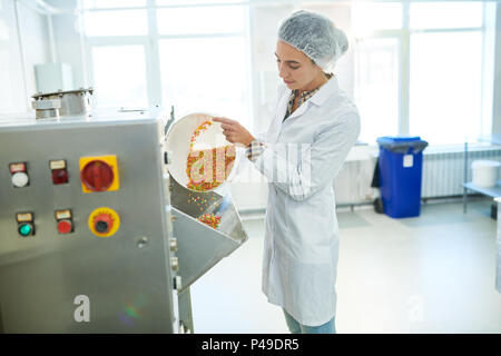 Confectionery factory worker pouring rainbow sprinkles into machine Stock Photo