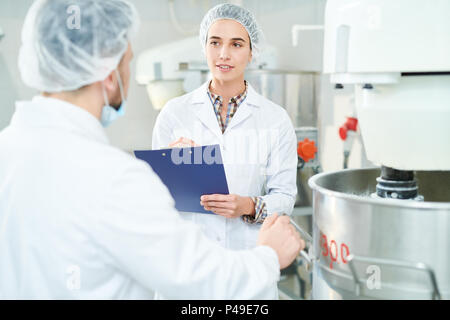 Confectionery factory worker taking notes talking to colleague Stock Photo