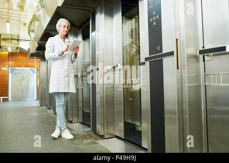 Woman standing in lab coat and using tablet Stock Photo