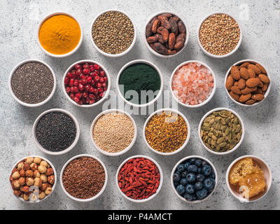 Various superfoods in smal bowl gray concrete background. Superfood as chia, spirulina, raw cocoa bean, goji, hemp, quinoa, bee pollen, black sesame, turmeric. Top view or flat-lay. Stock Photo