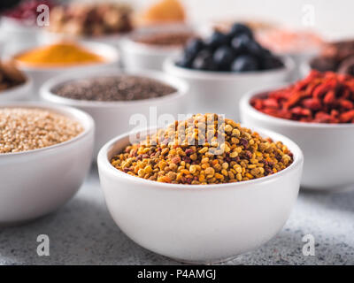 Bee pollen or beebread in small white bowl and other superfoods on background. Selective focus. Different superfoods ingredients. Concept and illustration for superfood and detox food Stock Photo